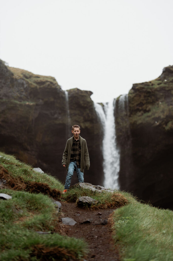 boy walks around Iceland waterfall during family photos with iceland photographer.