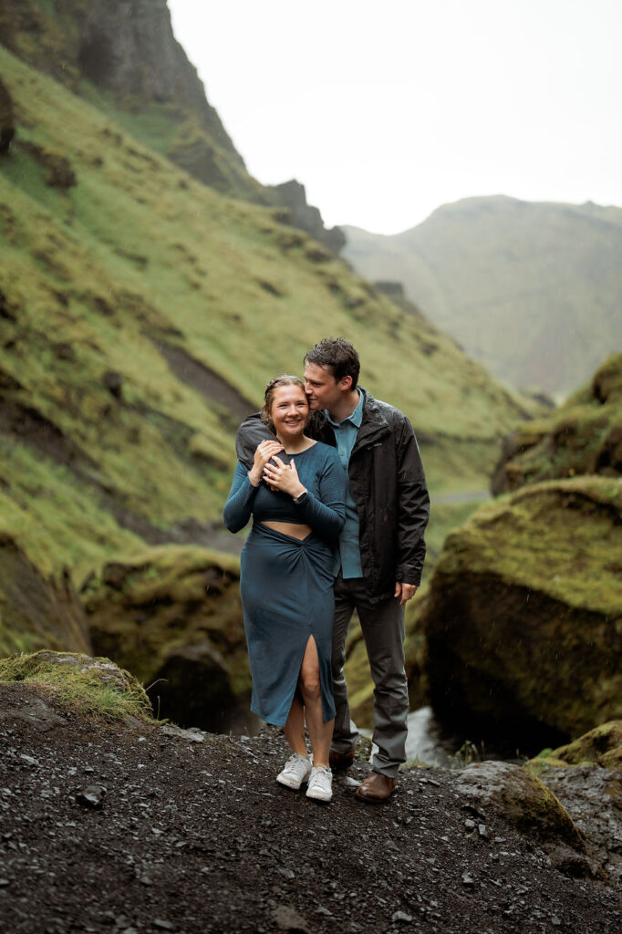 man wraps arm around woman with rocky and green valley in the background during iceland engagement photo shoot.