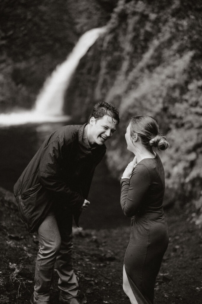 engaged couple smiles and laughs with waterfall in the background during iceland engagement pictures.