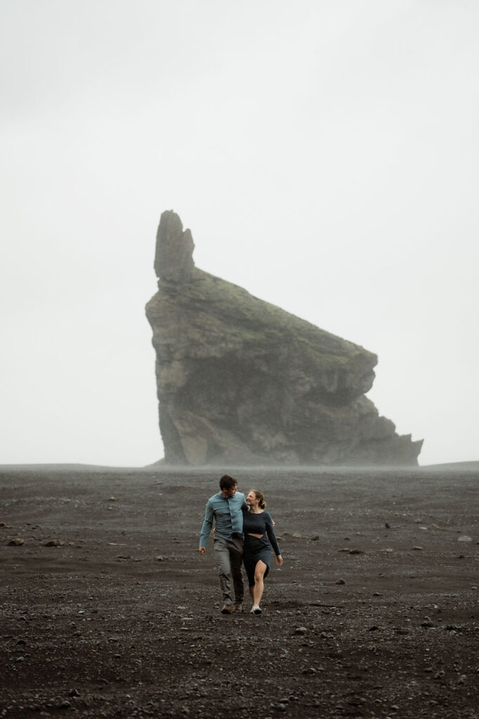 engaged couple walks down black sand beach during surprise proposal in Iceland.