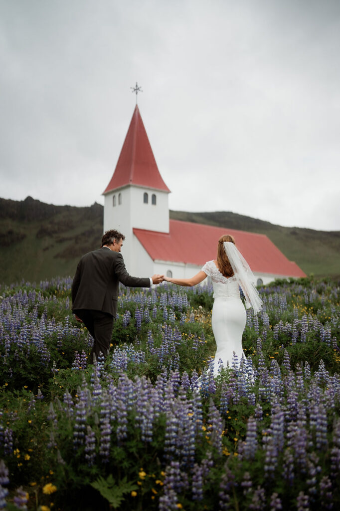 bride and groom getting married in iceland in front of Vik church and lupine fields