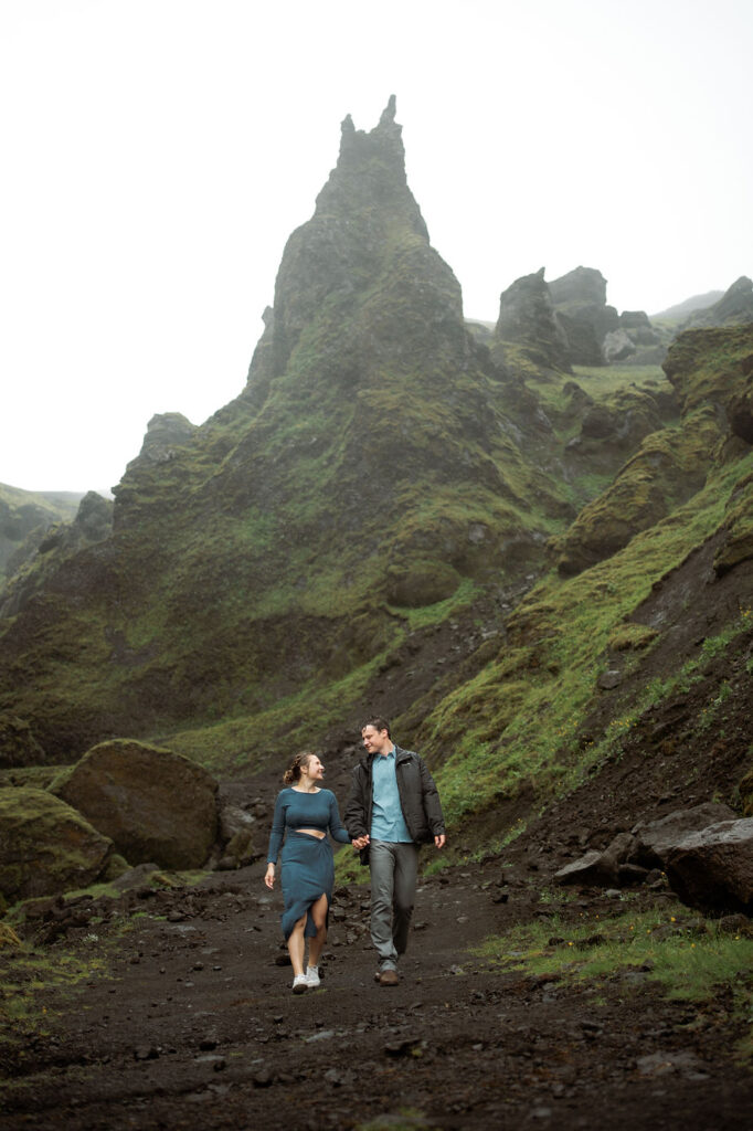 engaged couple holds hands and walks down valley during surprise iceland proposal photo shoot.