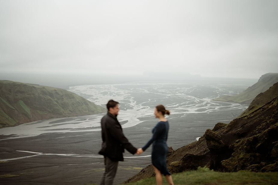 engaged couple holds hands with vast iceland valley in the background during proposal pictures.