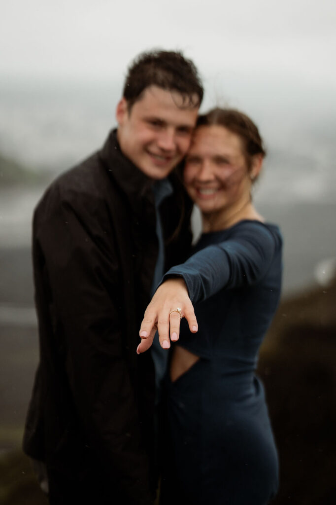 engaged couple hugs and wiman holds out hand, focusing on engagement ring, during adventure iceland proposal.