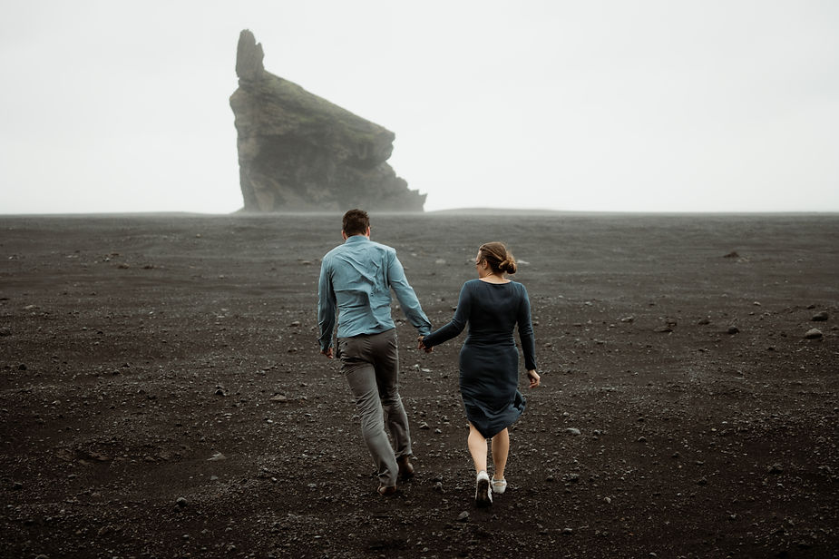 man and woman hold hands and walk down iceland coast during iceland engagement shoot with elopement planner.