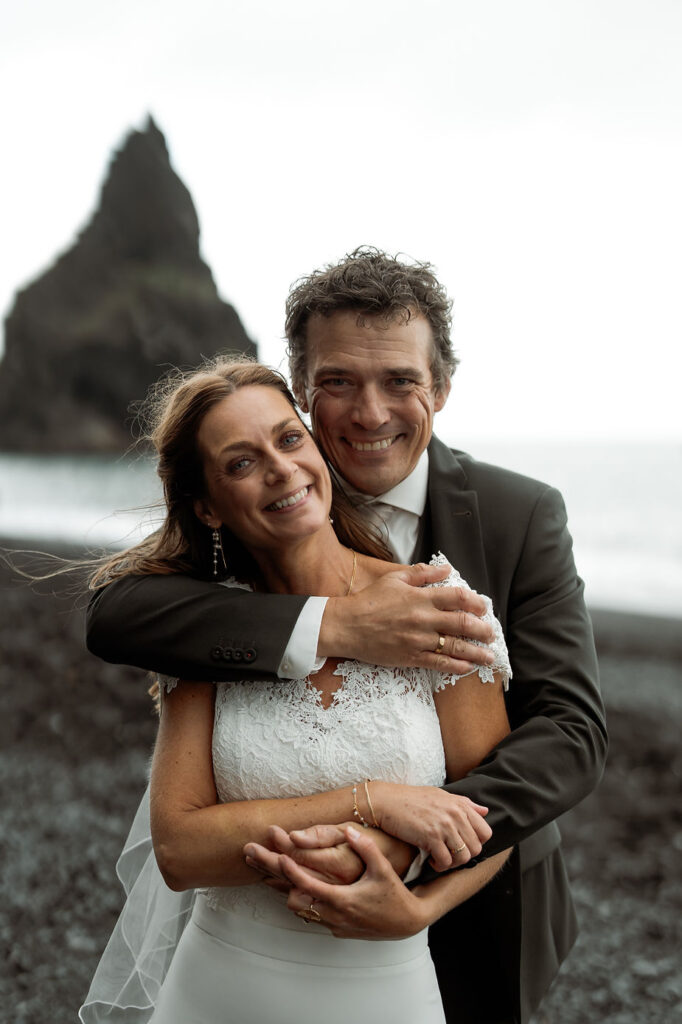 groom hugs bride from behind on iceland coast during iceland wedding photo shoot.