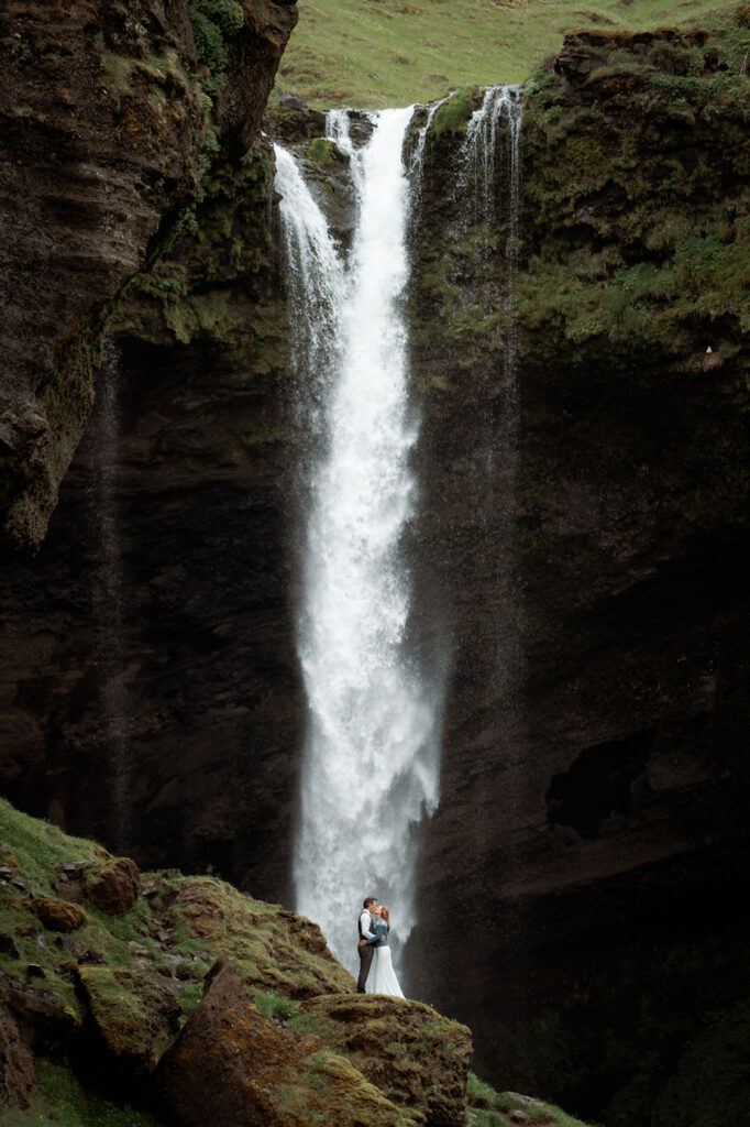 bride and groom kiss in front of waterfall during iceland adventure wedding.