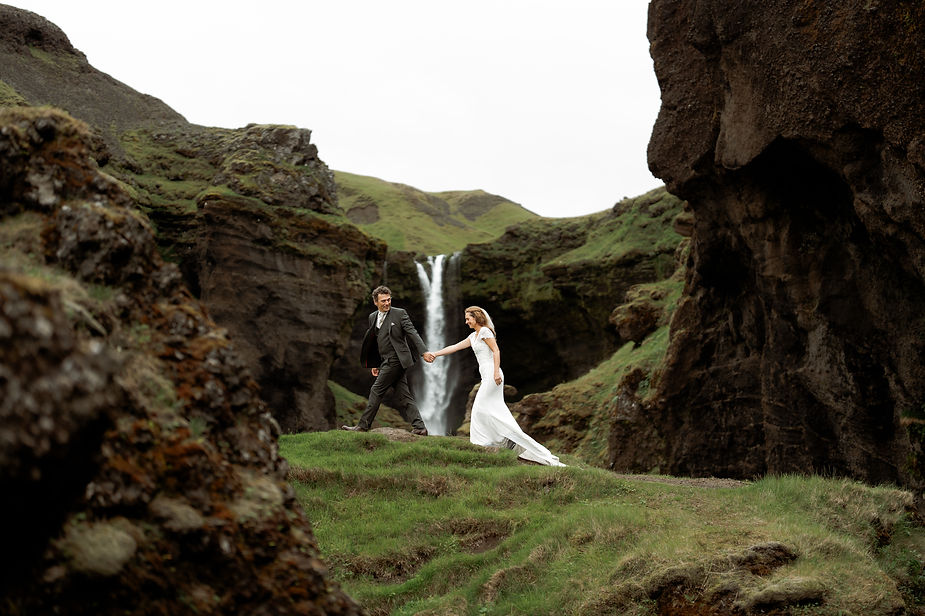 bride and groom walk across grassy ridge during photos with iceland wedding photographer.