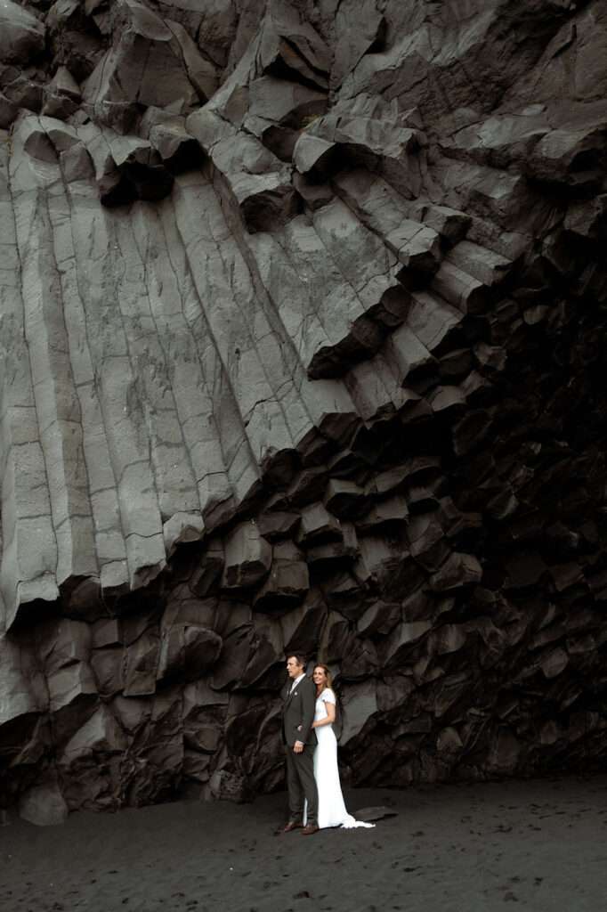 newlywed couple stands under rock formation during iceland wedding photos.