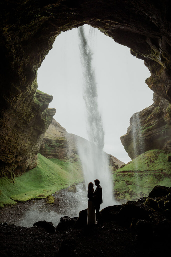 bride and groom stand behind waterfall during adventure iceland wedding.