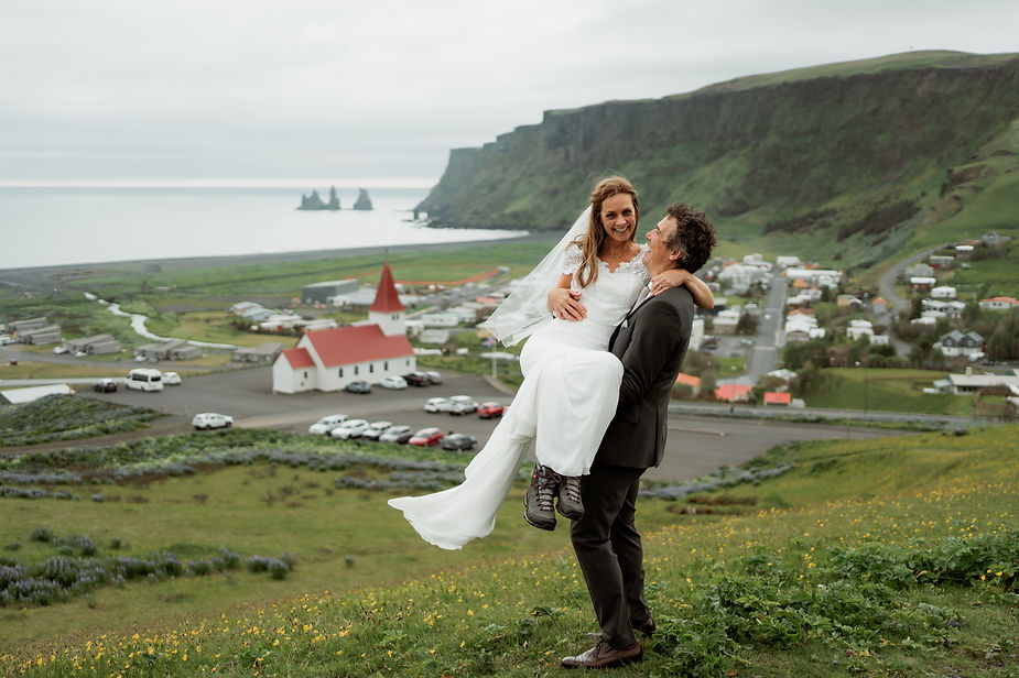 groom holds bride with town in the background during iceland intimate wedding photos.