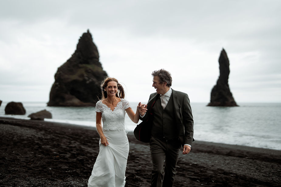 bride and groom run down black sand beach during iceland wedding photos.