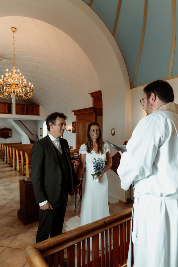 newlywed couple stands looking at priest during iceland church wedding ceremony.