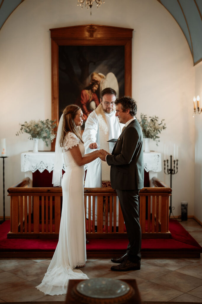 bride and groom stand in front of priest and smile during church iceland wedding ceremony.
