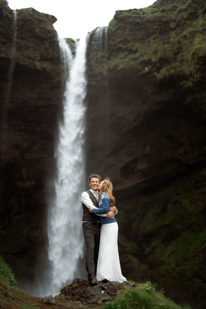 newlywed couple stands in front of waterfall during iceland wedding photo shoot.