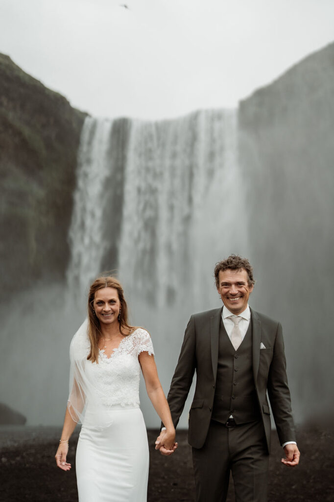 bride and groom walk away from waterfall during iceland adventure elopement.