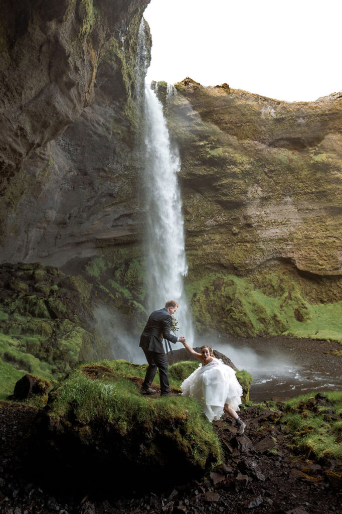 groom helps bride up rock during adventure elopement in iceland.