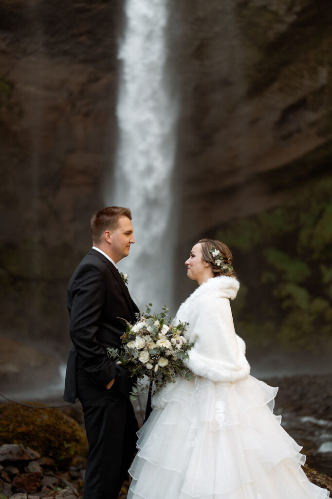 newlywed couple stands at the base of a waterfall during iceland wedding photos.