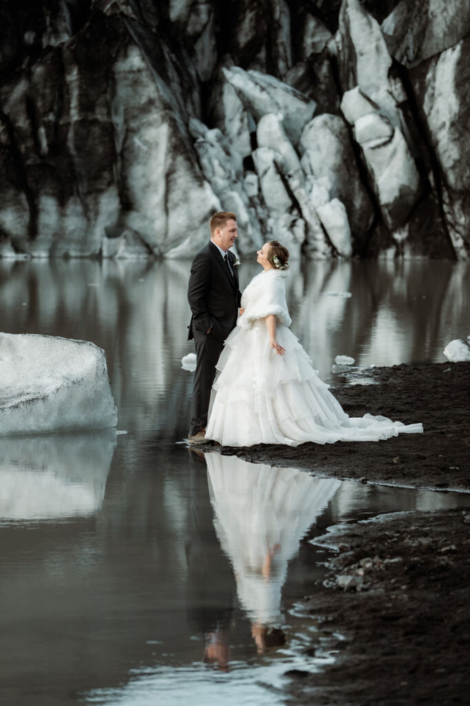 bride and groom stand at base of glacier during dreamy iceland wedding.