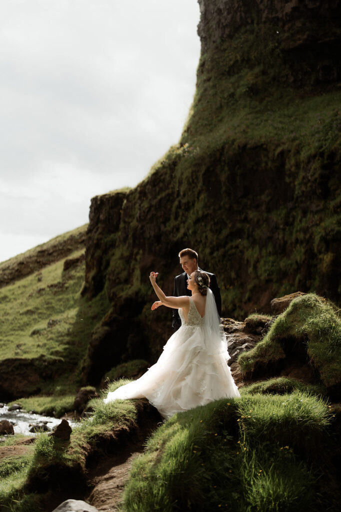 bride and groom stand in the sun, beside the cliff edge, during iceland wedding adventure.