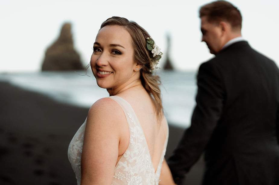 bride looks back as bride and groom walk down coast during iceland elopement.