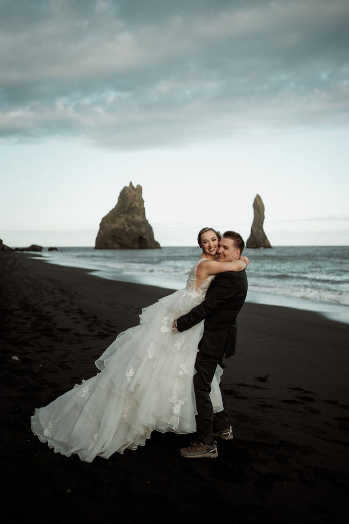 groom lifts up bride on black sand beach in iceland during dreamy wedding elopement.