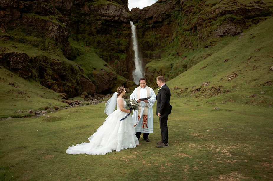 bride and groom get married by priest in front of waterfall during iceland wedding ceremony.
