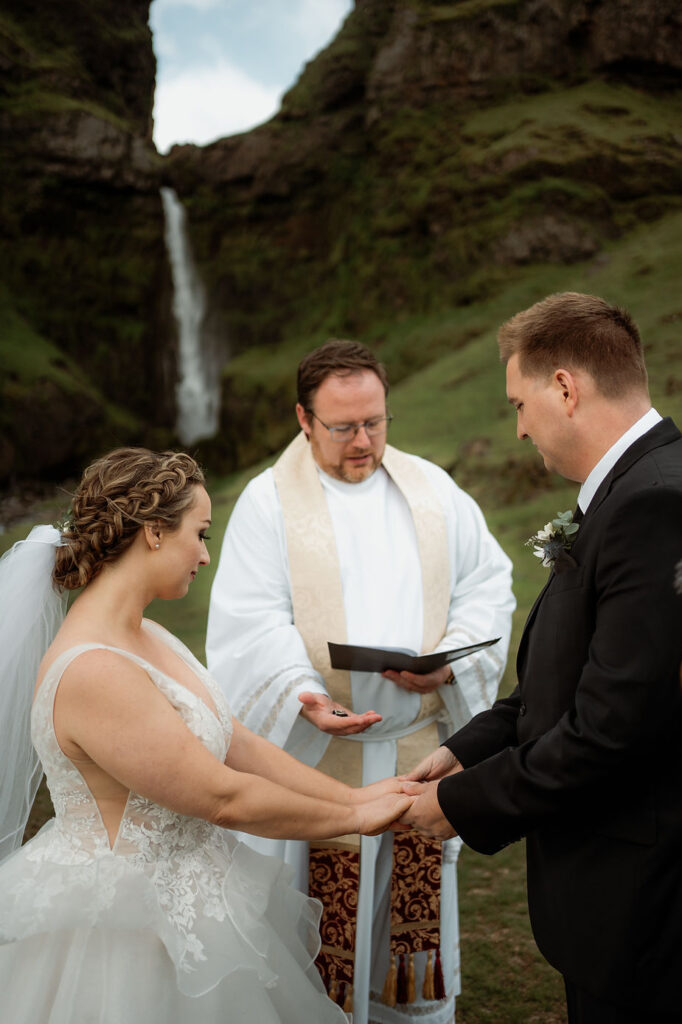 bride and groom get married by priest in front of waterfall during iceland wedding ceremony.