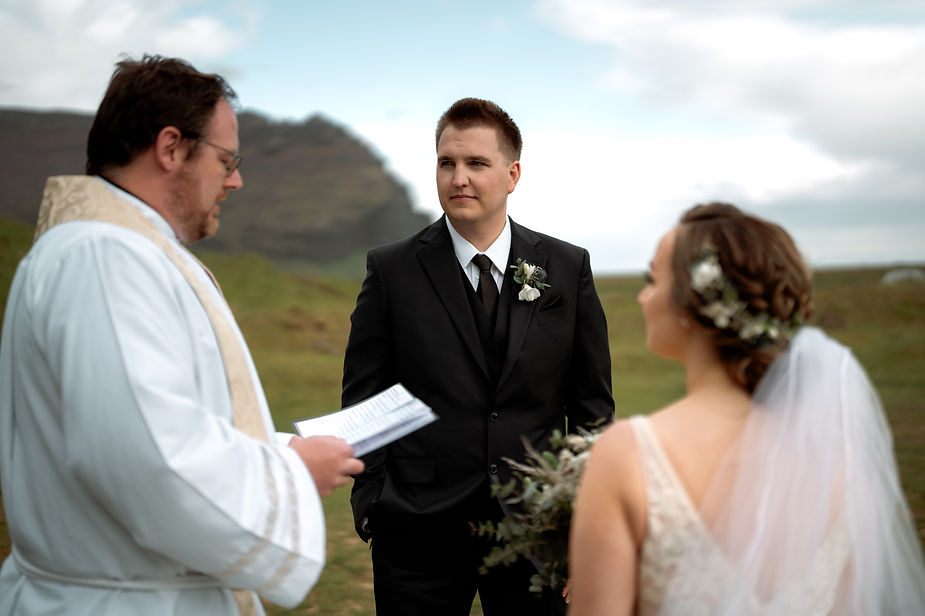 bride and groom look at priest during outdoors wedding ceremony in iceland.