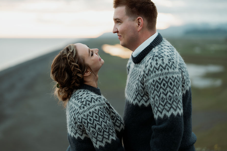 newlywed couple stands on cliff edge looking at each other during iceland wedding portraits.
