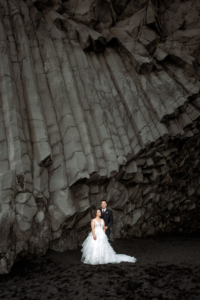 bride and groom stand under rock formation during adventure elopement in iceland.