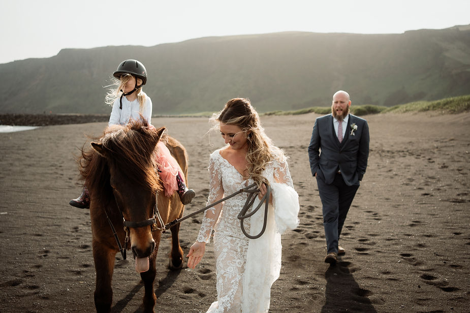 bride, groom, and daughter ride a horse on the beach in iceland during adventure wedding photos.