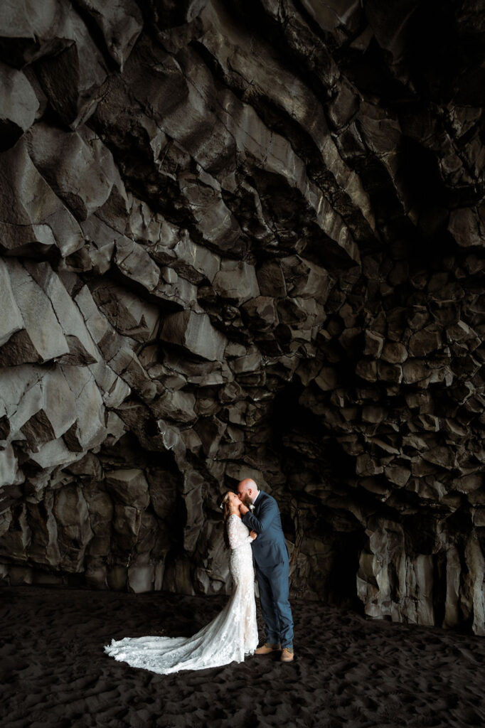 bride and groom kiss under black rock formation during iceland wedding.
