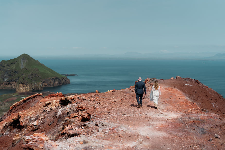 bride and groom walk towrds cliff egde during westman islands wedding.