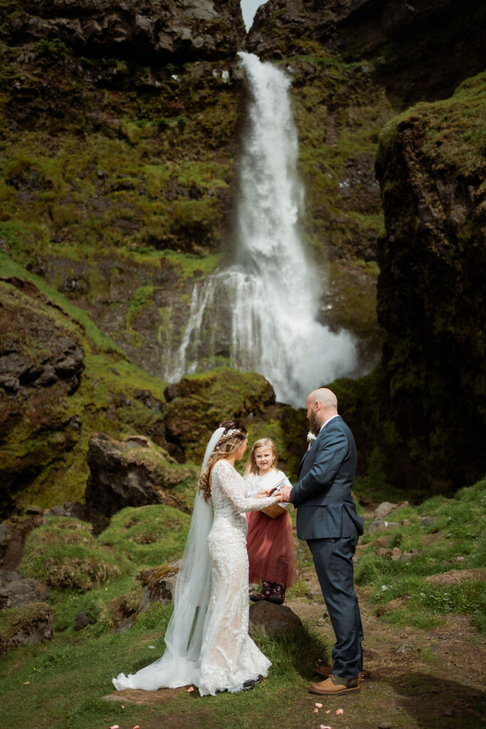 Bride and groom and daughter stand at the bottom of a waterfall during iceland adventure wedding in the westman islands.