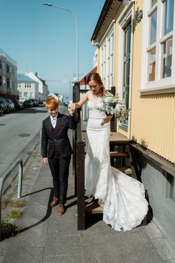 lgbtqi couple holds hands and walks down steps of a house during iceland wedding photos.