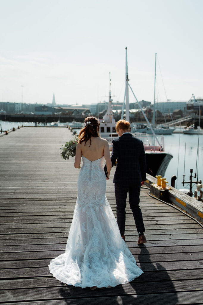 partners walk hand in hand down the harbour in reykjavik during their iceland wedding photos.