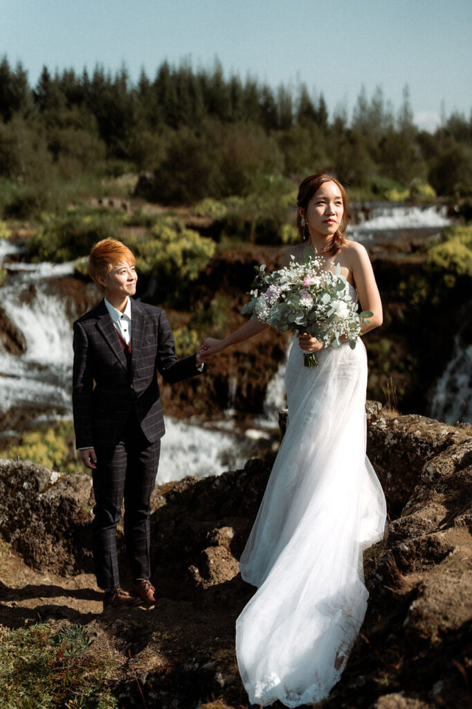 lgbtqi+ couple stands on grassy rocky area in reykjavik during iceland wedding photos.