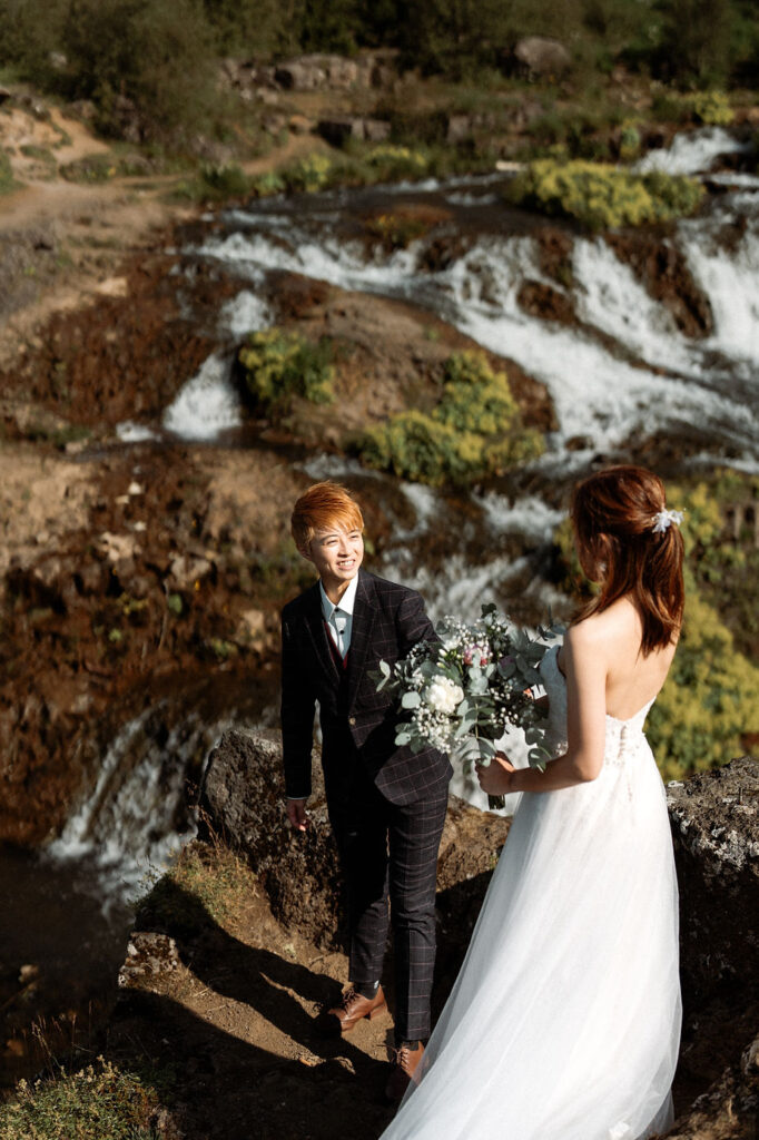 lgbtqi+ couple stands on grassy rocky area in reykjavik during their destination wedding photos in iceland.