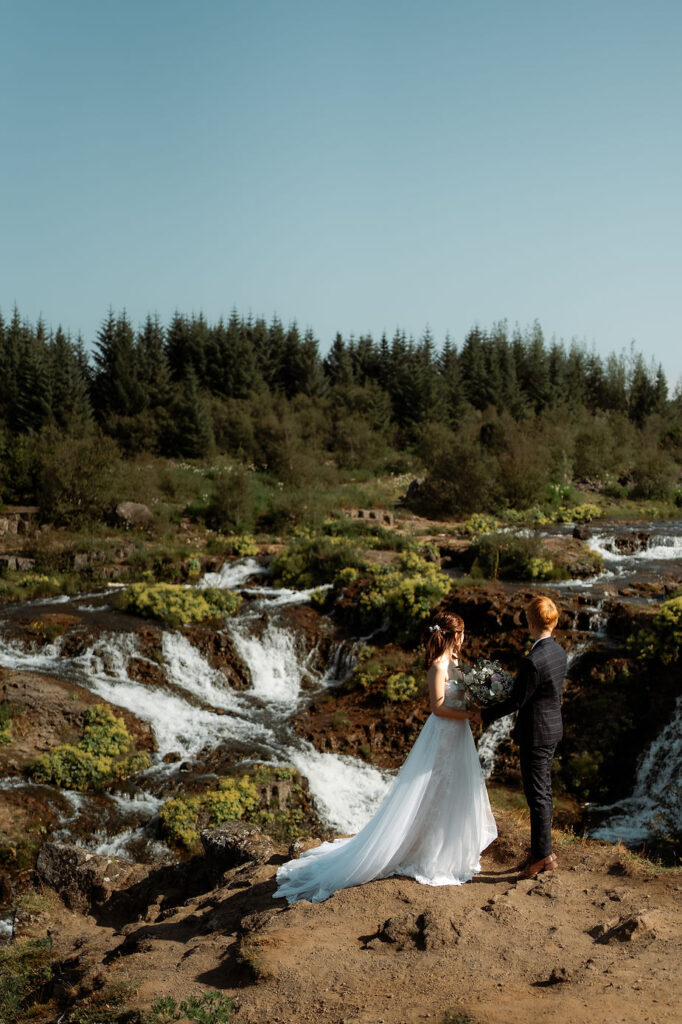 lgbtqi+ couple stand on grassy ledge in reykjavik during their iceland wedding photos.