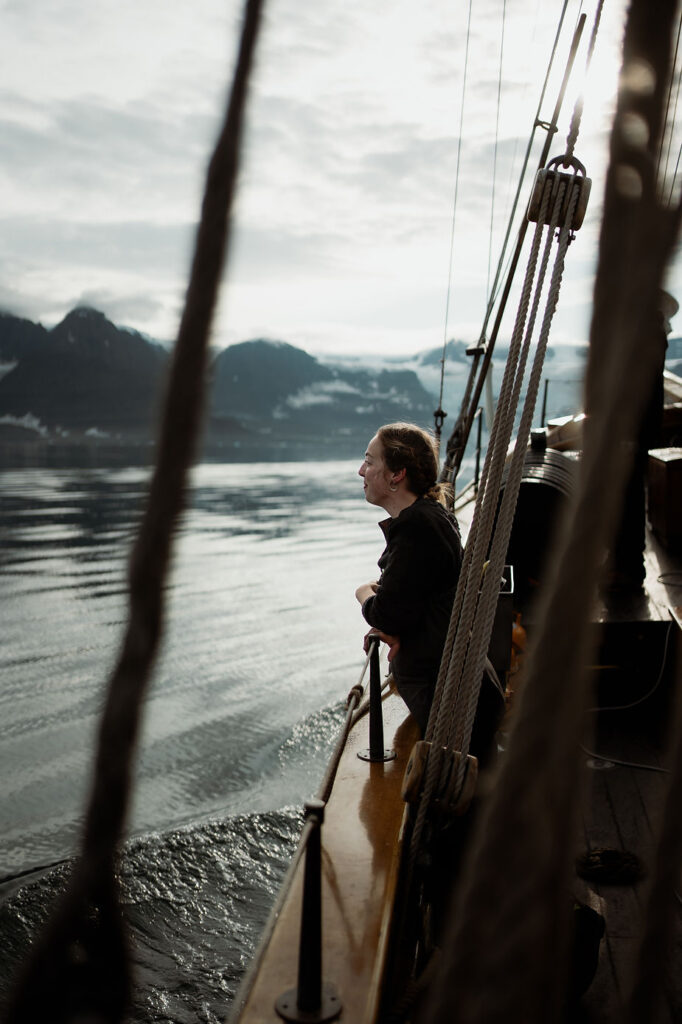 woman leans over edge of sailboat during adventure elopement in greenland.