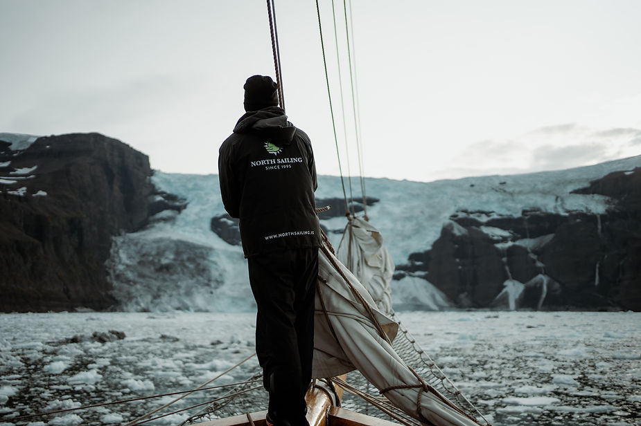 man stands on the front of a sailboat during destination wedding in greenland.