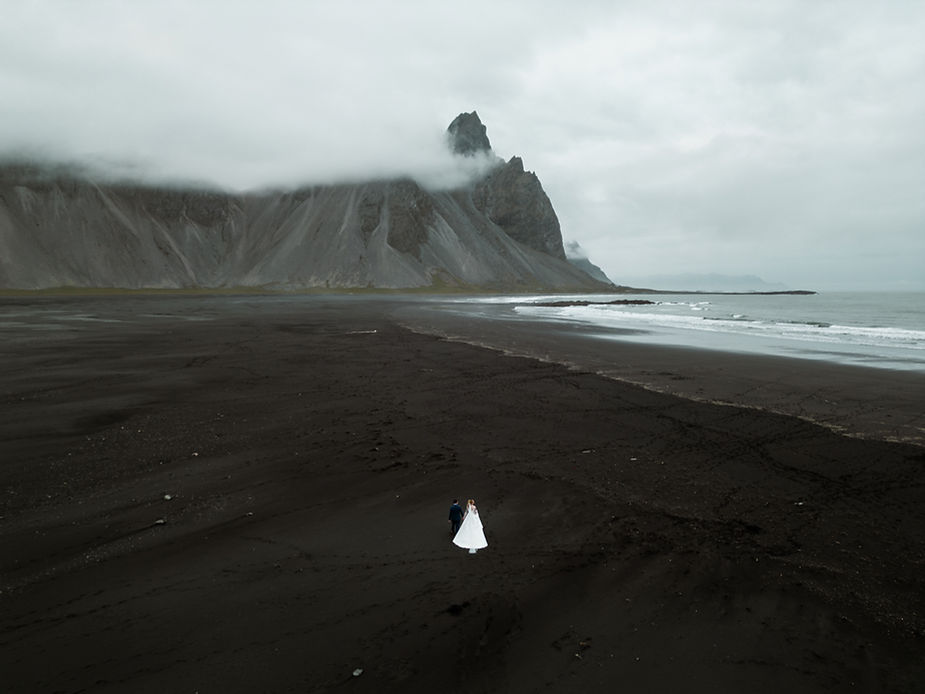 bride and groom walk along black sand beach during iceland wedding adventure.