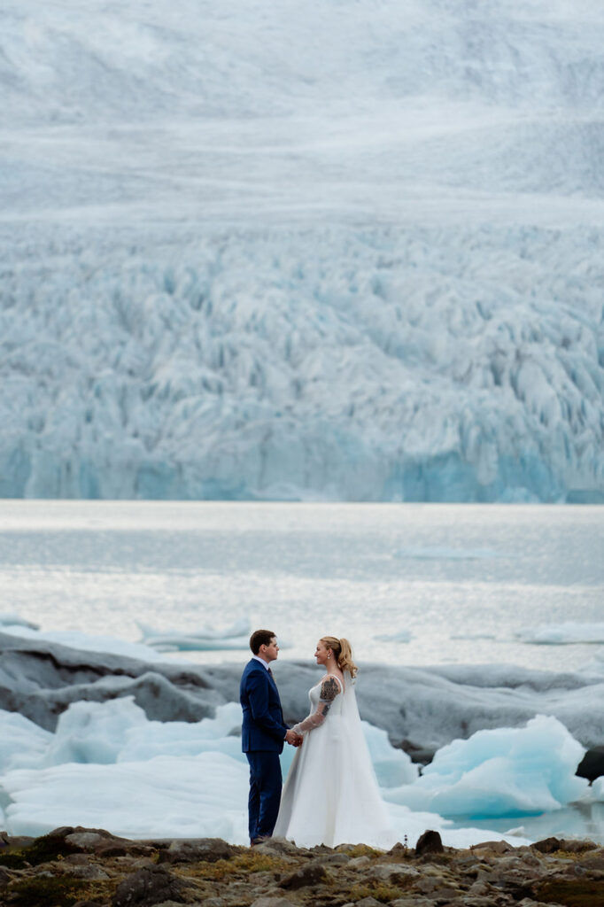 bride and groom stand at base of glacier during iceland wedding.