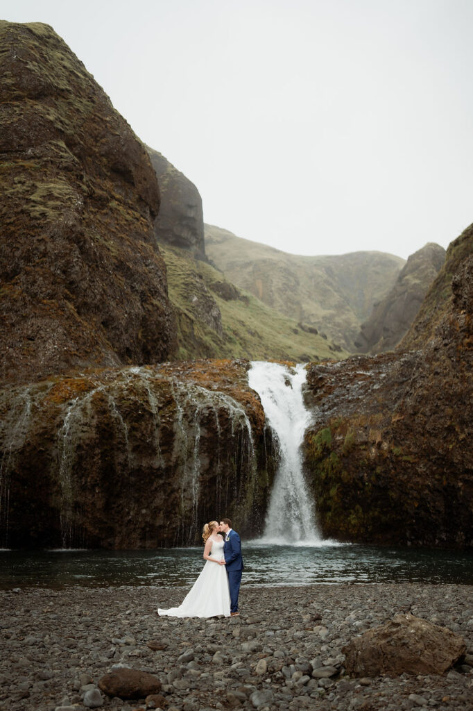 bride and groom kiss at waterfall during iceland wedding adventure.