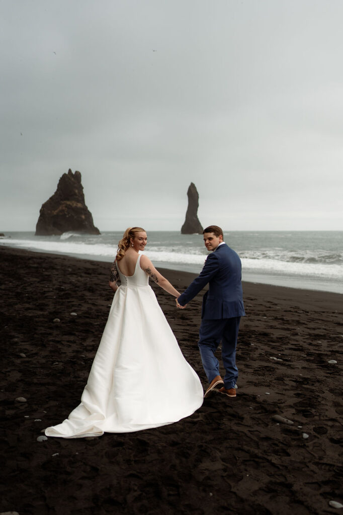 bride and groom walk along black sand beach during perfect iceland wedding day.