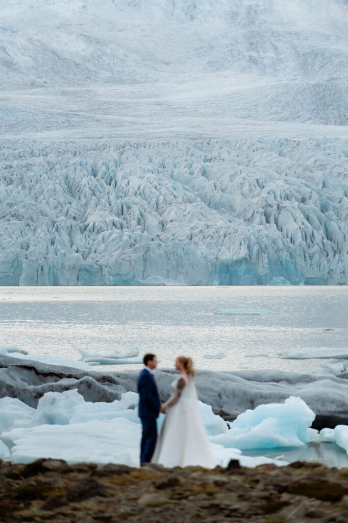 bride and groom stand at base of glacier during iceland wedding adventure.