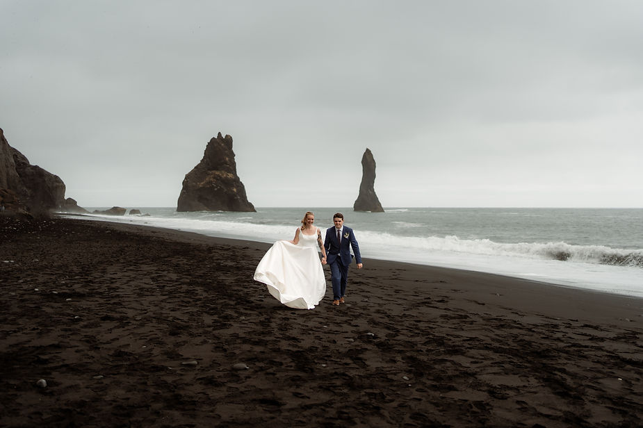 bride and groom walk along black sand beach during adventure wedding in iceland.
