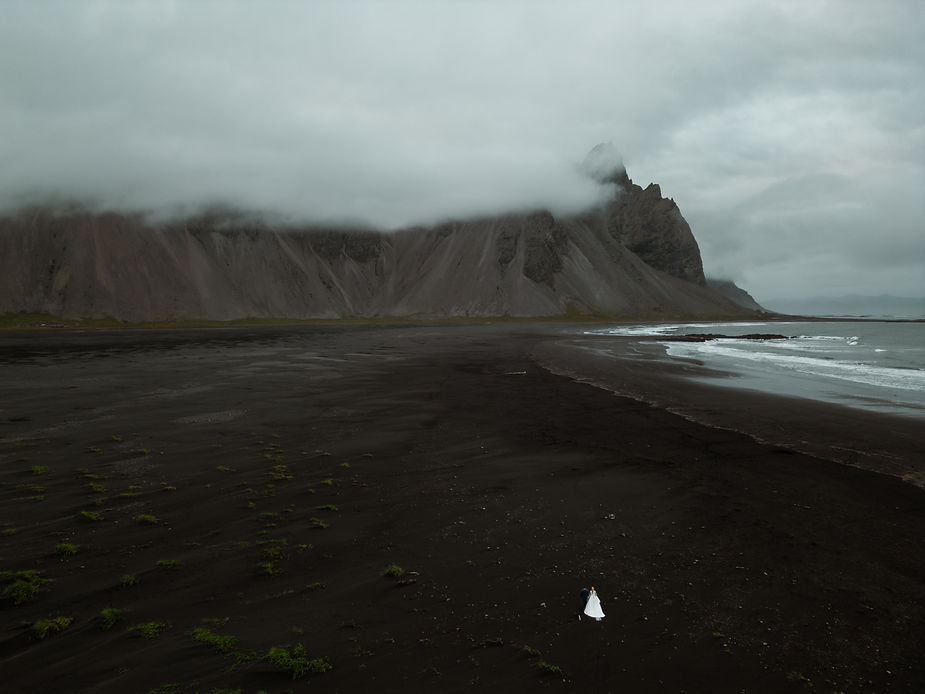 bride and groom walk along black sand beach during iceland wedding day.