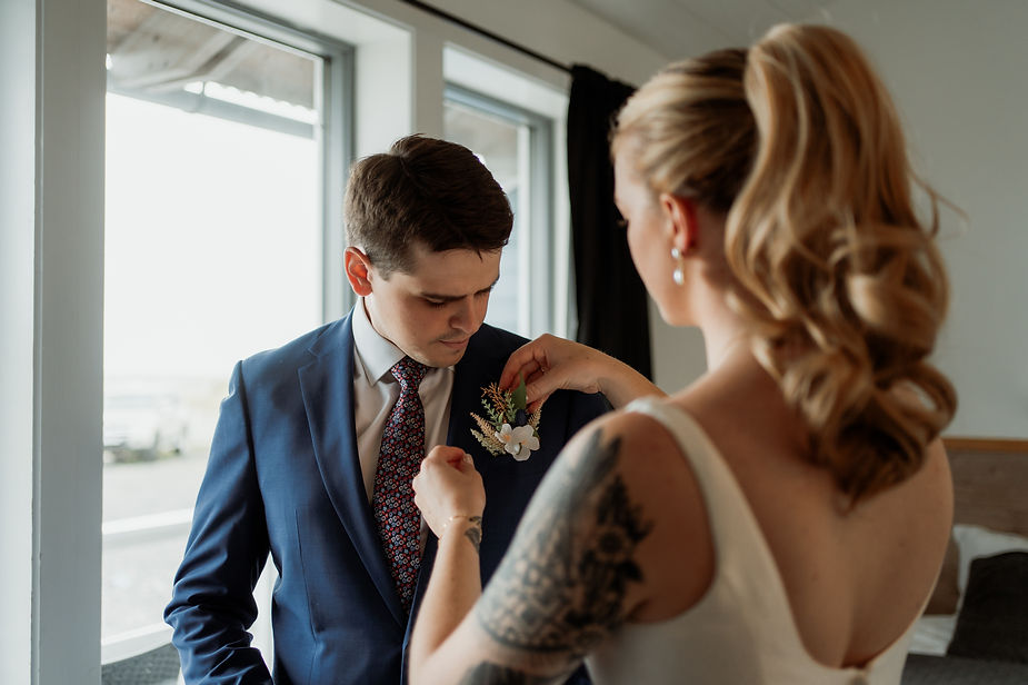 Bride puts flowers on groom in preperation for their adventure wedding with iceland wedding photographer.